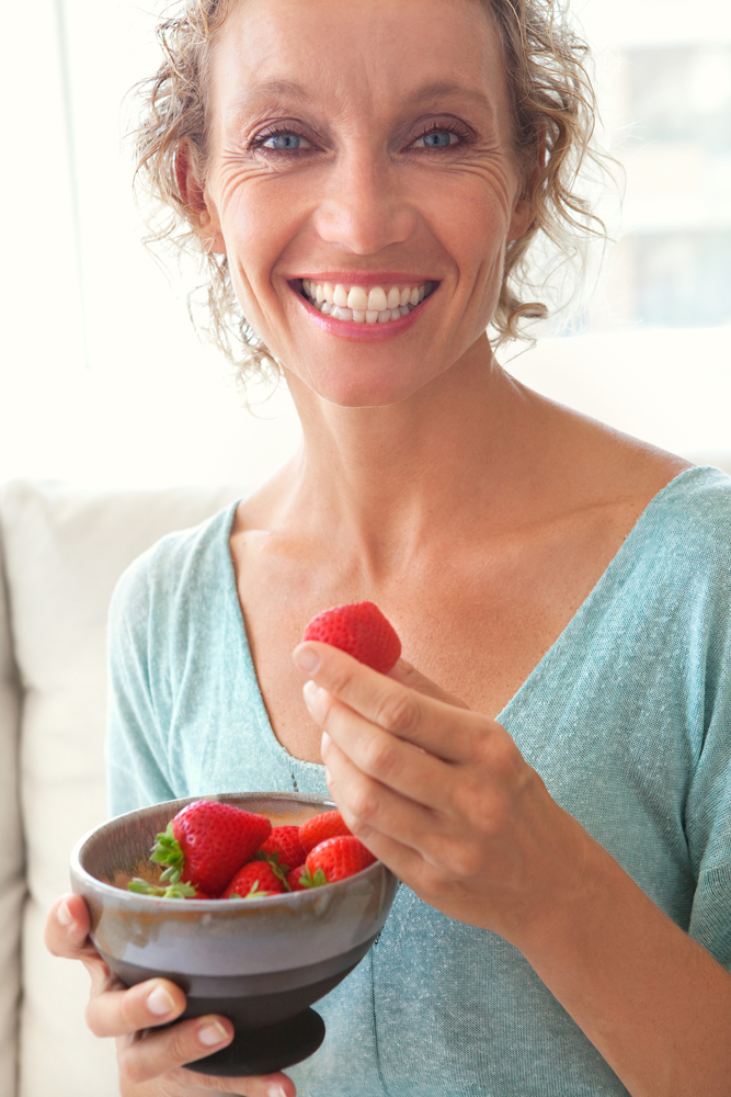 Woman enjoying strawberries with a healthy smile supported by dental implants